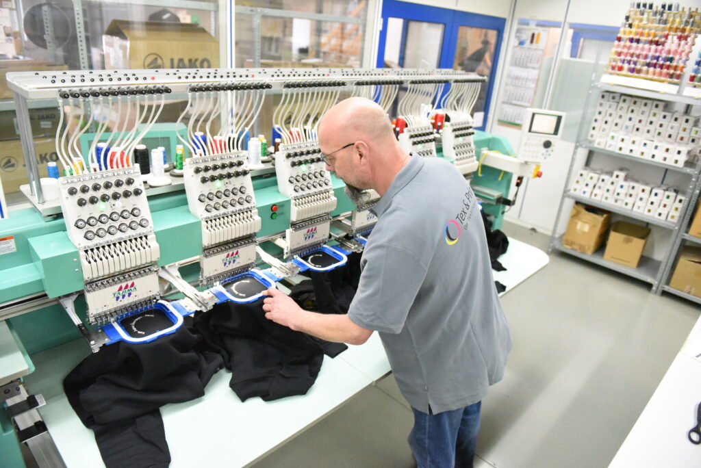 Stickmaschine bei Tex & Print: Ein Mitarbeiter richtet Pullover im Stickrahmen aus
